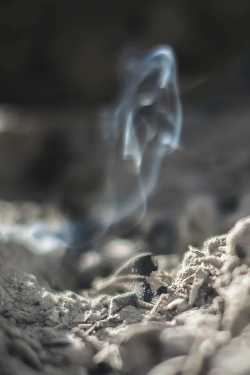 Wisps of smoke rising above ash and charred embers